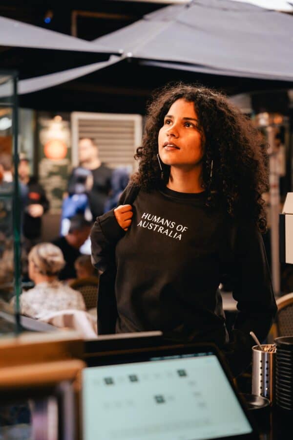 A stunning image of a beautiful woman wearing the Humans of Australia Black Jumper, showcasing its elegant fit and versatile style.