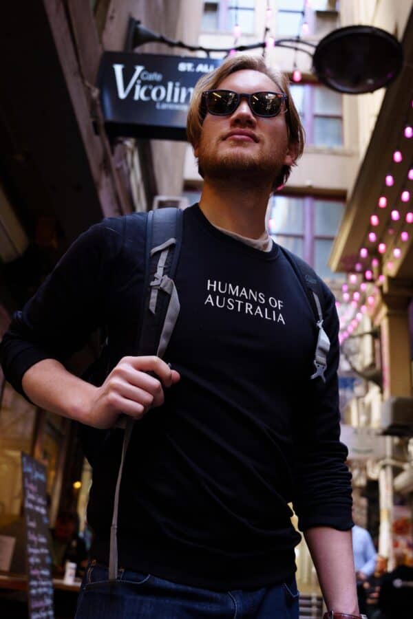 A man carrying a backpack and wearing the versatile Humans of Australia Black Jumper.